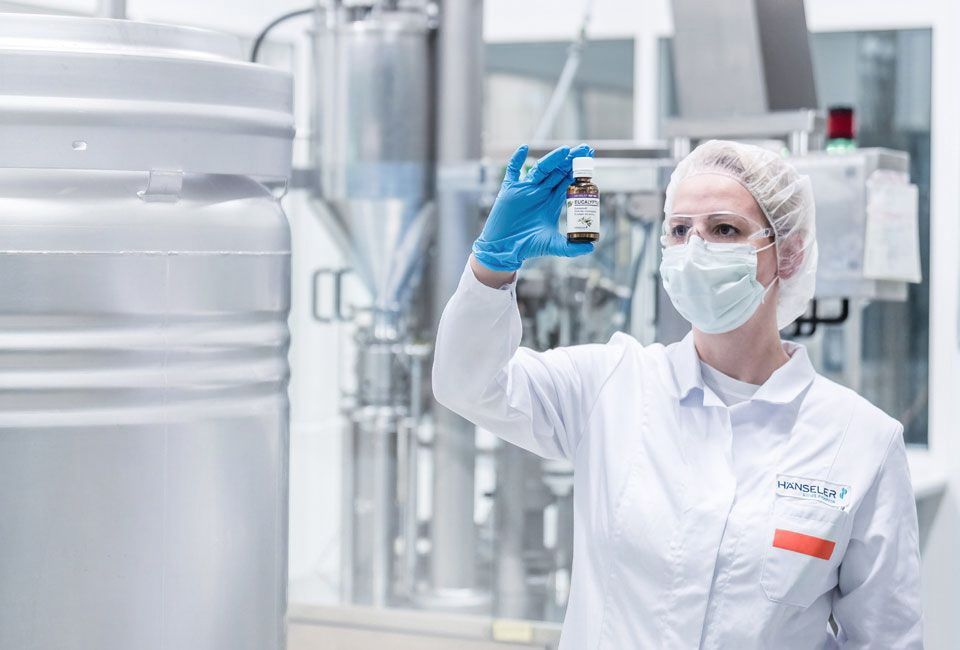 Eine Mitarbeiterin von Hänseler in Schutzkleidung prüft im Labor eine Flasche