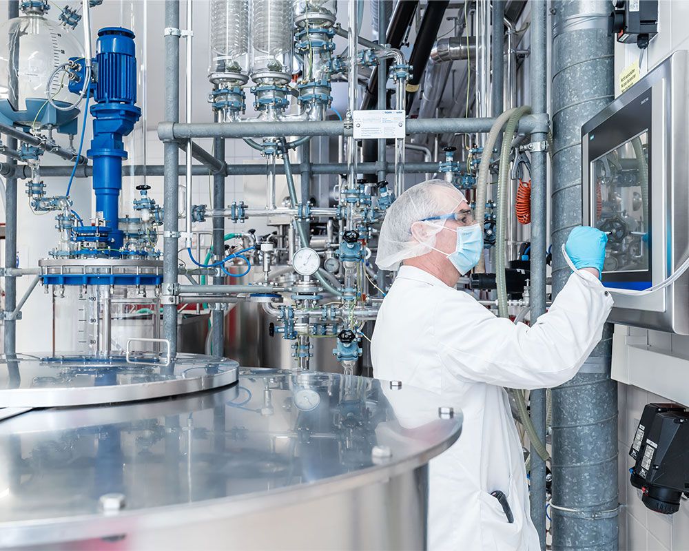 Un homme travaillant dans la production, vêtu de vêtements de protection, se tient devant une installation de distillation et utilise le tableau de commande.